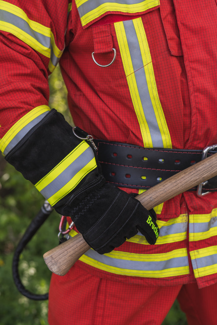 Feuerwehrmann hält mit rechts mit Feuerwehrhandschuhen S Black einen Axtstiel am unteren Ende