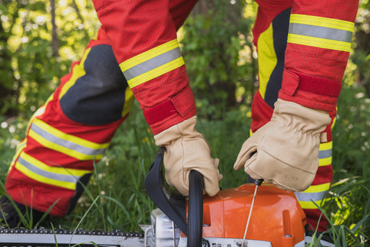 Feuerwehrmann hält die Einsatzhandschuhe Pro tragend mit rechts eine Kettensäge und zieht mit links am Startersteil